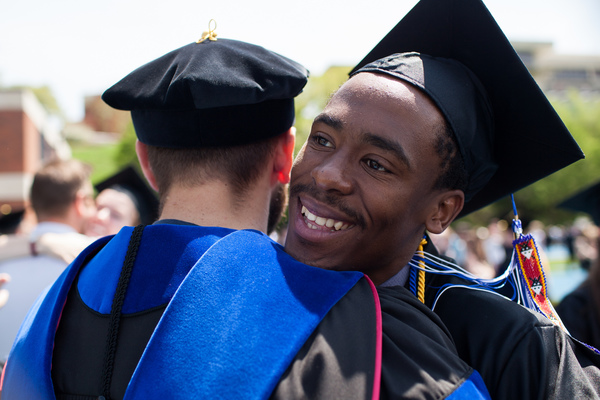 A 2014 graduate hugs a professor while wearing his cap and gown after the commencement ceremony.