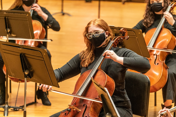 A cello student playing with a mask on in a Symphony concert.