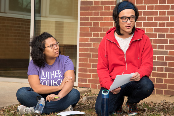 Students and their professor hold a class discussion outside.