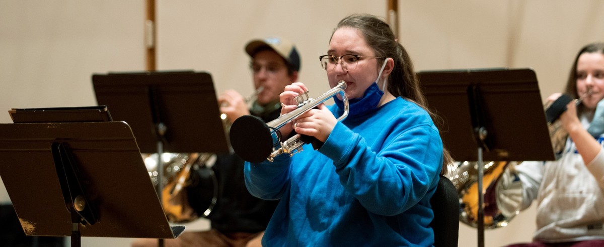 A student playing the trumpet with a mask and trumpet bell cover.